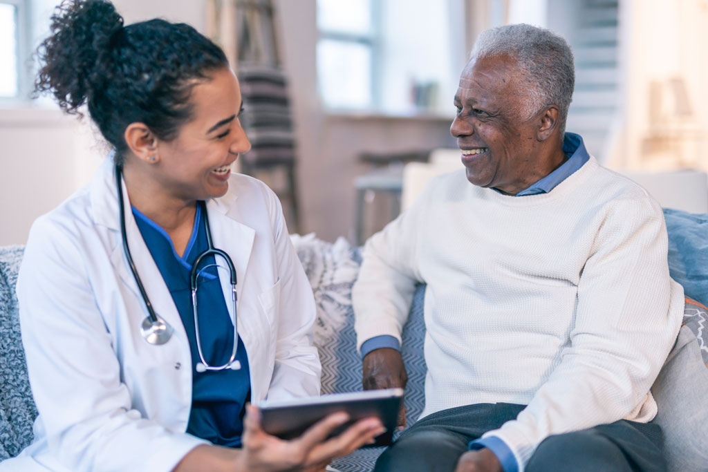 Smiling female medical provider sitting next to smiling older male patient